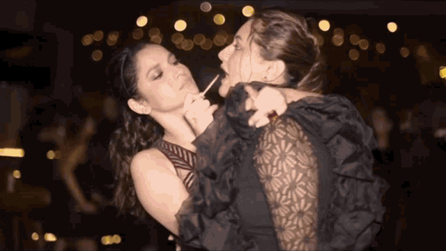 a couple of women standing next to each other with one holding a cigarette
