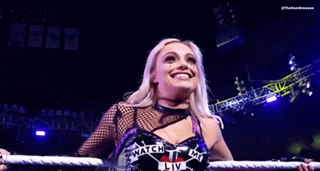 a woman is standing in a wrestling ring holding a rope and looking up .