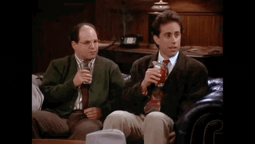 two men are sitting on a couch drinking from glasses of beer .