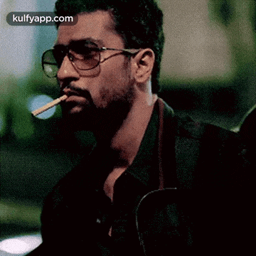 a man wearing glasses is smoking a cigarette in his mouth .