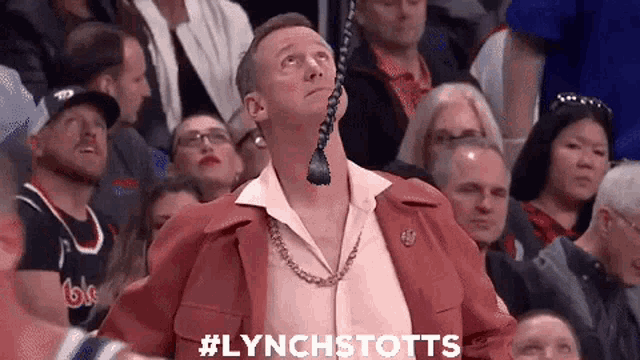 a man wearing a tie looks up at the sky while watching a basketball game in a crowd .