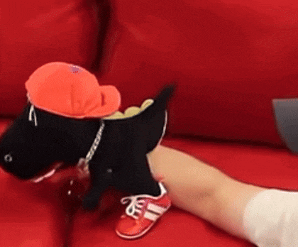 a person is sitting on a red couch with a stuffed dog wearing a hat and sneakers