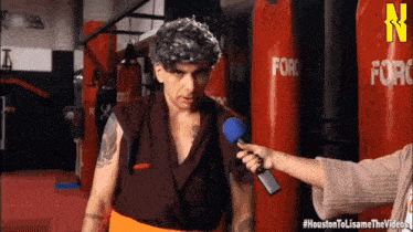 a man with gray hair is being interviewed by a woman with a microphone in front of red punching bags that say force