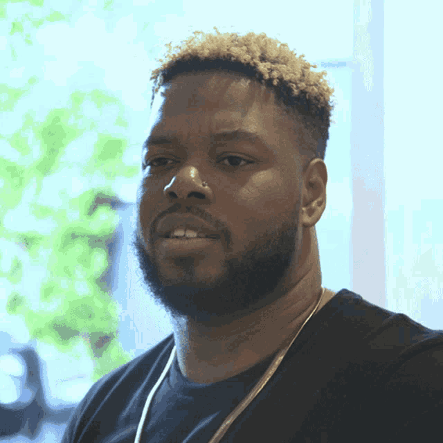 a man with a beard is wearing a black shirt and a gold necklace