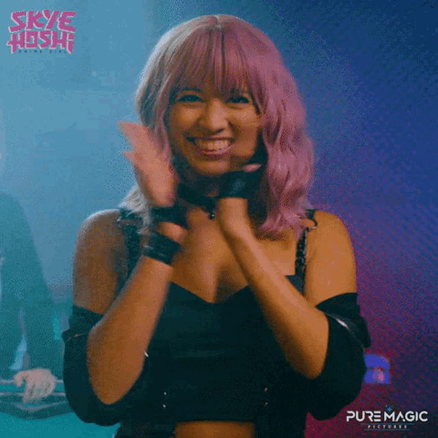a woman with pink hair is clapping her hands and smiling