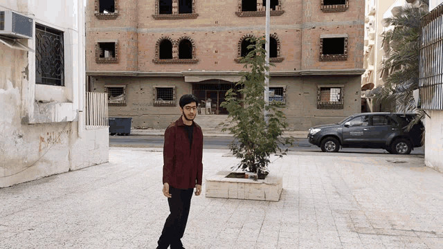 a man in a red shirt stands in front of a building with a car parked in front of it that says toyota hilux