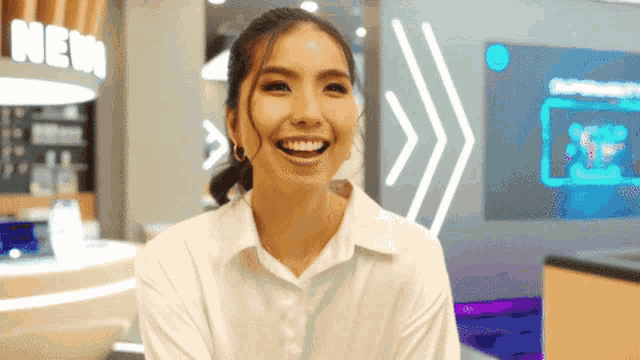 a woman in a white shirt is smiling in front of a sign that says new