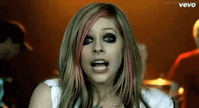 a woman with pink and green hair is making a funny face in a video for vevo .