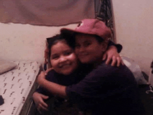 a boy wearing a pink hat is hugging a girl on a bed