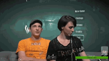 a man and a woman are sitting on a couch in front of a computer screen that says new game