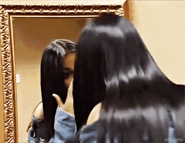 a woman with long black hair is looking at herself in a mirror ..