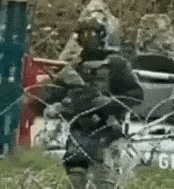 a soldier is walking through barbed wire while holding a gun in a field .