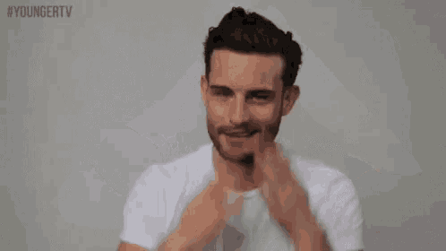 a man with a beard wearing a white t-shirt is holding his arms up in the air .