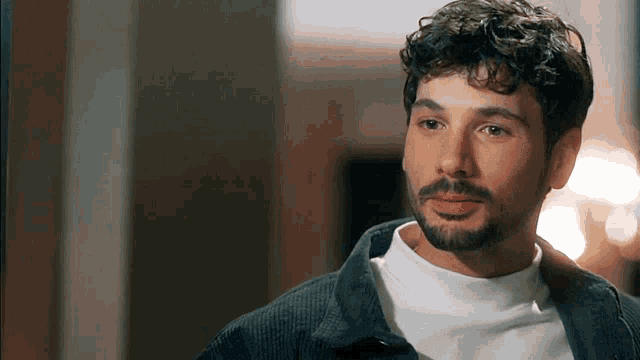 a man with a beard is wearing a white sweater and a black jacket .