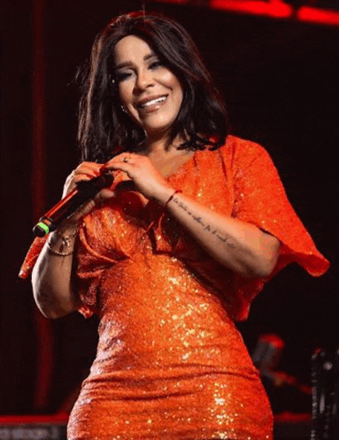 a woman in an orange dress is holding a microphone and smiling