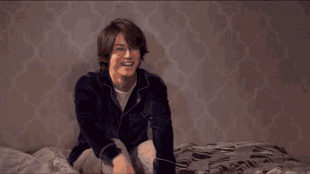 a man in pajamas sits on a bed smiling