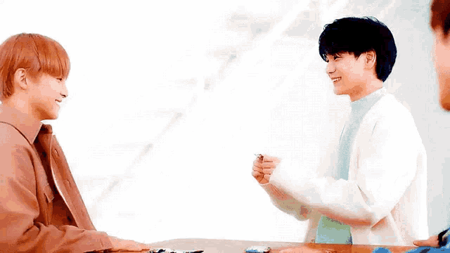 two young men are sitting at a table talking to each other and laughing .