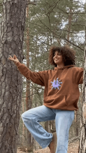 a woman in a brown hoodie stands next to a pine tree