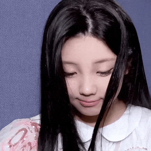 a woman with long black hair is wearing a white shirt and looking down