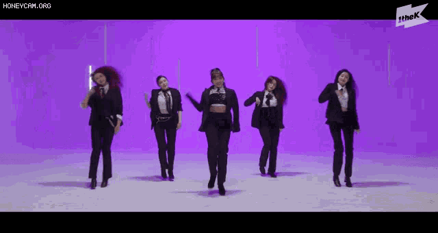 a group of women in suits and ties are dancing in a purple room .