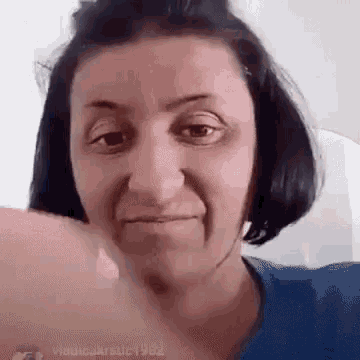 a woman in a blue shirt is making a funny face while giving a thumbs up .