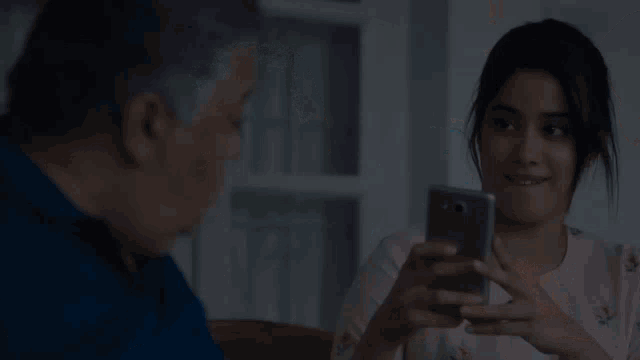a man in a blue shirt is looking at a woman holding a cell phone