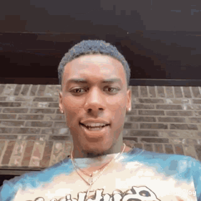a young man wearing a tie dye shirt and a necklace is smiling .