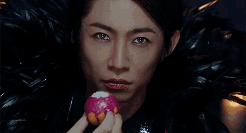 a man in a black feathered cape holds a pink apple in his hand