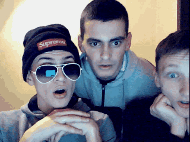 a man wearing a supreme hat and sunglasses poses with two other men