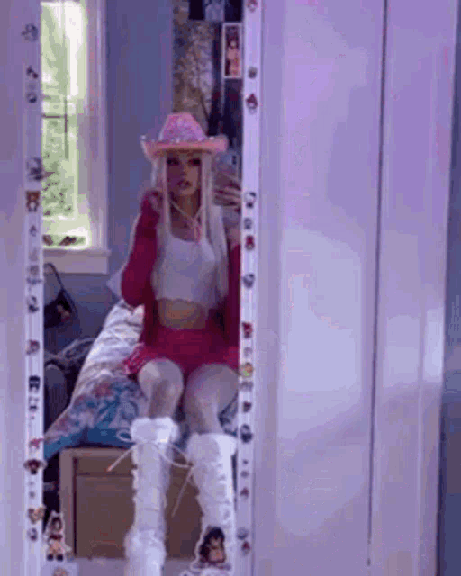 a girl is taking a selfie in front of a mirror while wearing a cowboy hat .