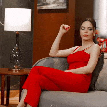 a woman in a red jumpsuit sits on a couch