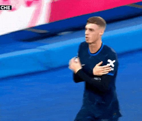 a man wearing a blue shirt with an x on the sleeve is standing on a blue surface