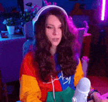 a woman wearing headphones and a colorful hoodie is sitting in front of a microphone in a room .