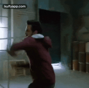a man in a red hoodie is standing in a room holding a stick .