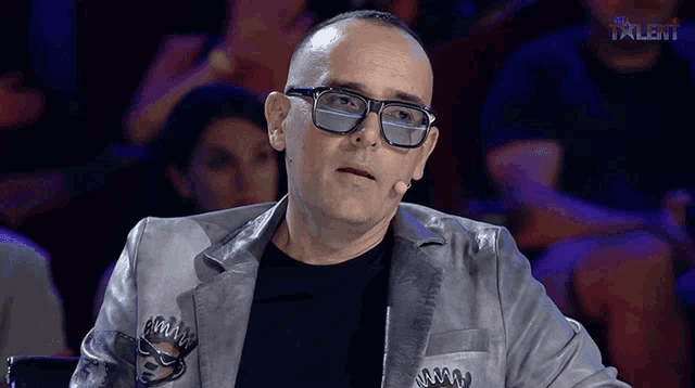 a man wearing glasses and a jacket with the word talent in the corner