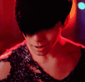a close up of a woman 's face in a dark room with red lights behind her .