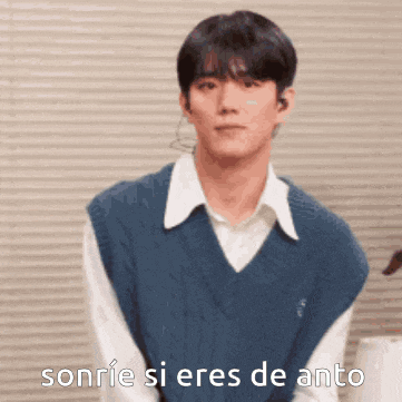 a young man wearing a blue vest and a white shirt is smiling and says sonrie si eres de anto .