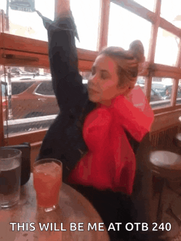 a woman in a red jacket sits at a table with a glass of orange juice