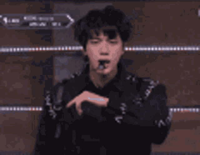 a man in a black jacket is holding a microphone in his mouth and pointing at something .