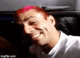a man with pink hair and a white shirt is smiling