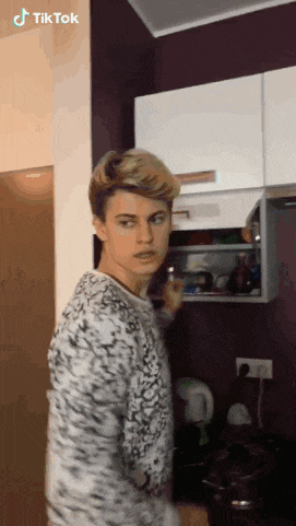 a young man is standing in a kitchen with a purple wall behind him and a tiktok logo on the bottom right