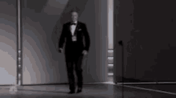 a man in a tuxedo is walking towards a microphone on a stage