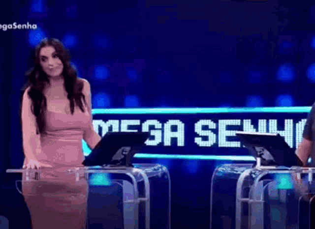 a woman in a pink dress is standing in front of a mega senha sign .