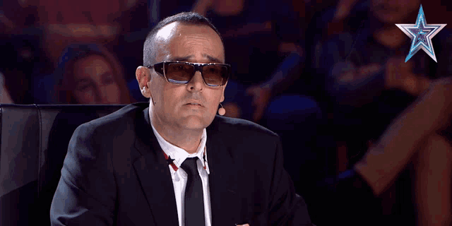 a man wearing sunglasses and a suit is sitting in front of a blue star