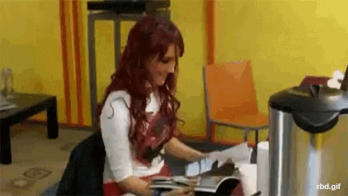 a woman with red hair is sitting at a table reading a magazine .
