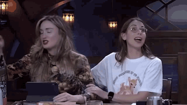 two women are sitting at a table and one of them is wearing a t-shirt that says i 'm a unicorn