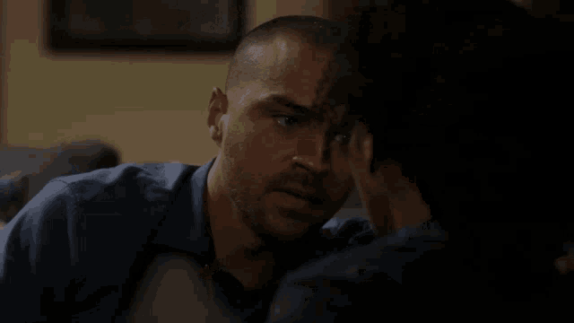 a man in a blue shirt looks at a woman in a dark room