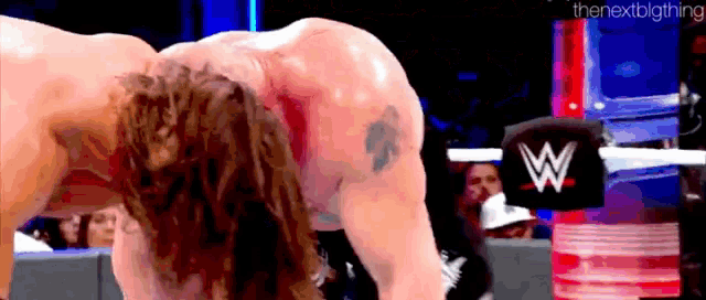 a man is bending over in a wrestling ring with a w logo on the ring .
