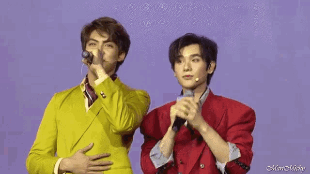 two men in suits are standing next to each other on a stage . one of the men is holding a microphone .