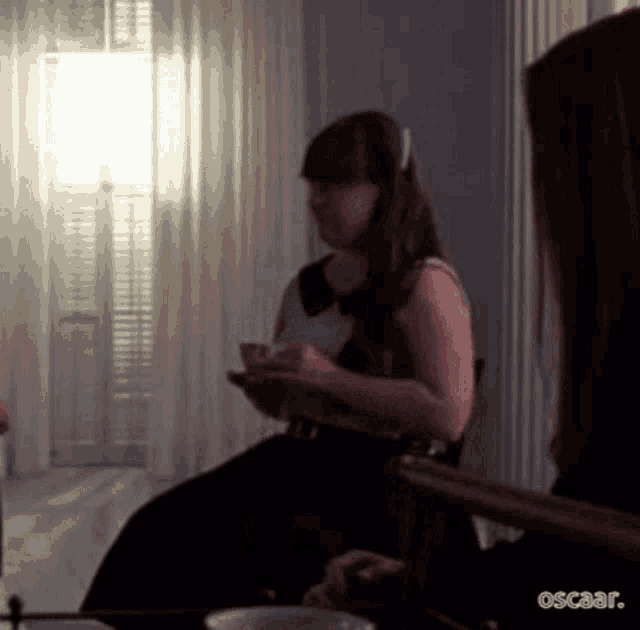 a woman in a black dress is sitting in a chair holding a cup of tea .
